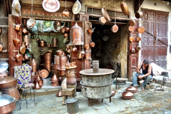 Boutique artisanale avec divers objets en cuivre, homme assis à l'intérieur.