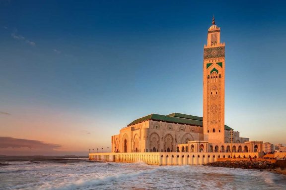 Mosquée Hassan II à Casablanca, avec un phare et des vagues au crépuscule.